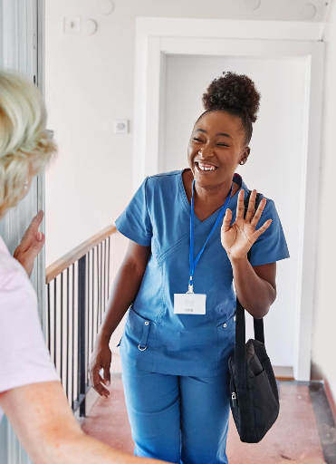 A nurse warmly greeting an elderly woman at the door.