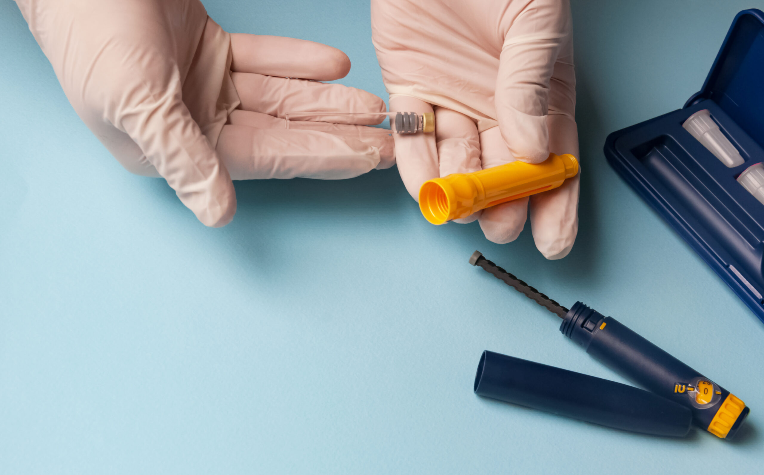 Hands holding a yellow pill bottle with a prescription label, next to an insulin pen.