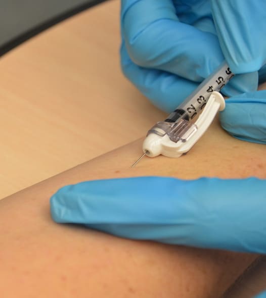 Gloved hands administering an injection in arm.